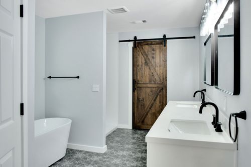 A bright, modern bathroom featuring a white soaking tub, double vanity with black fixtures, and a rustic barn door.