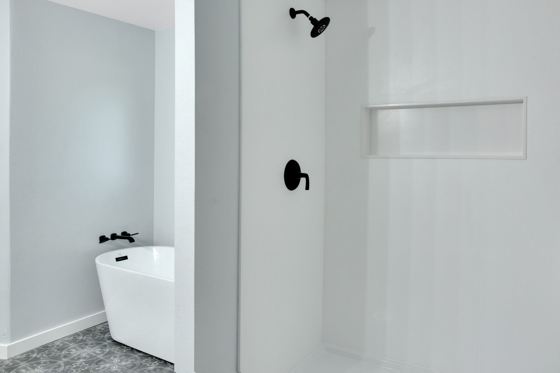 A modern bathroom featuring a white soaking tub and a walk-in shower with black fixtures against light gray and white walls.