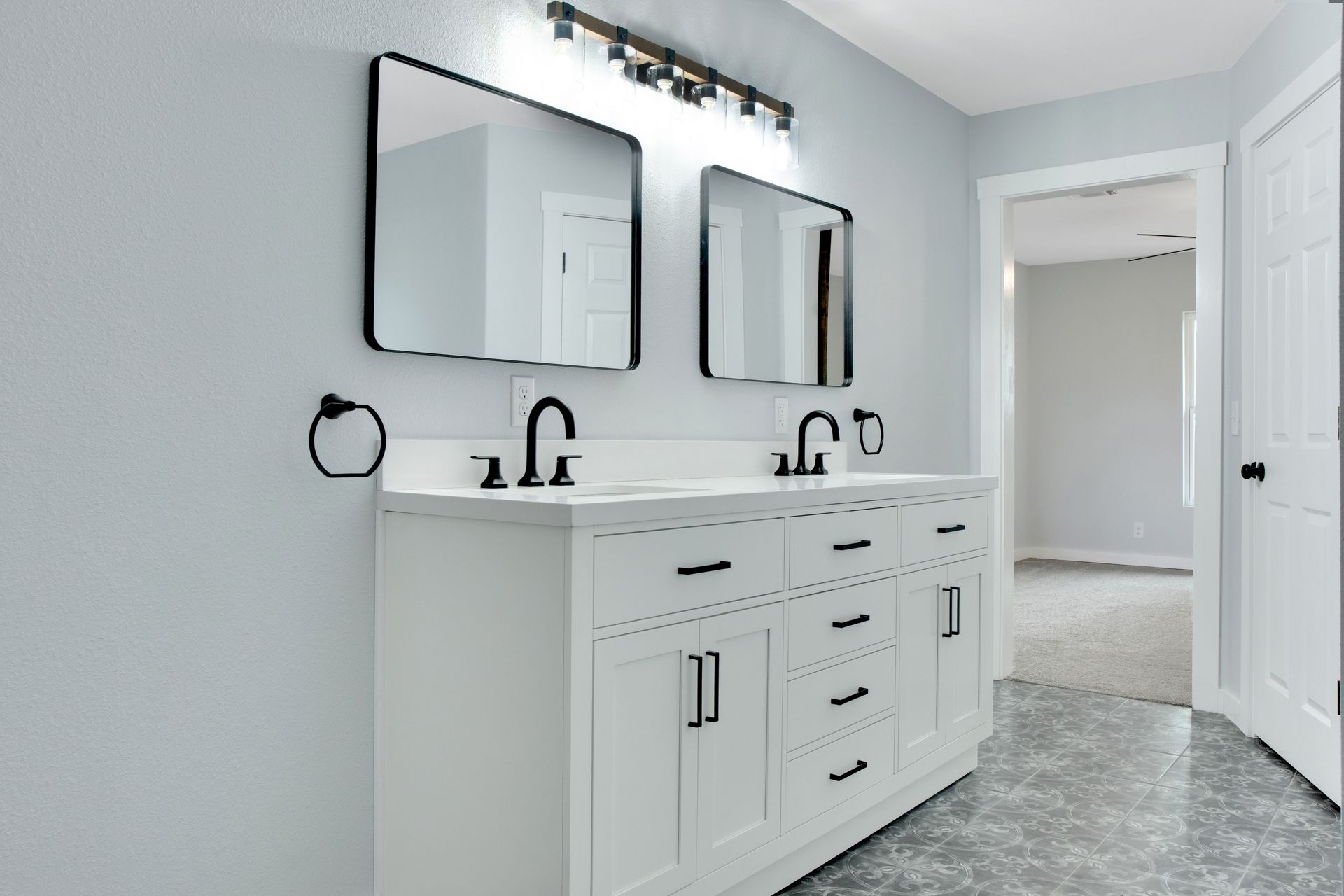 A modern bathroom vanity with dual sinks, white cabinets, black hardware, two mirrors, and overhead lighting.