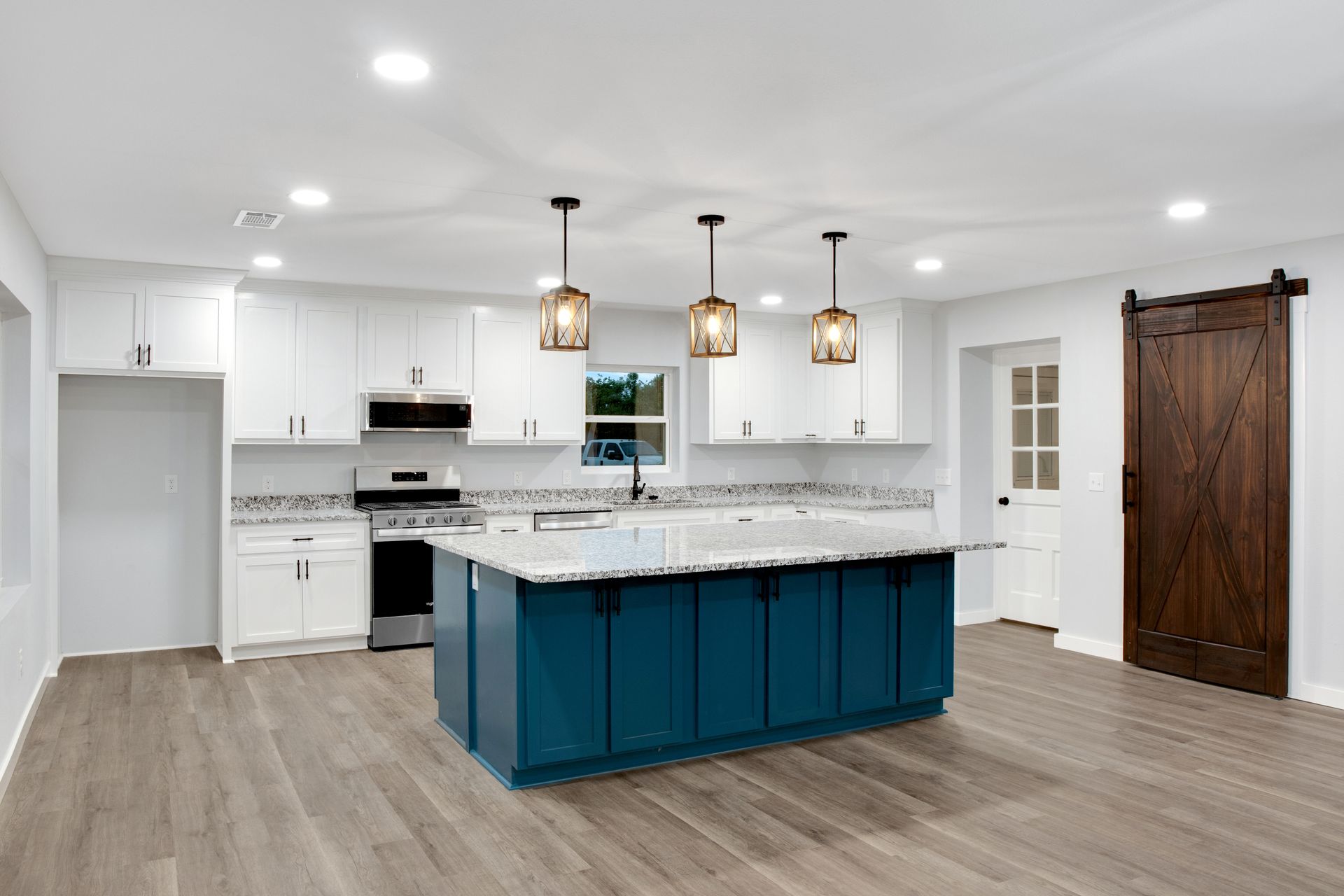 Modern kitchen featuring a blue center island, white cabinetry, granite countertops, and a dark wood barn door.