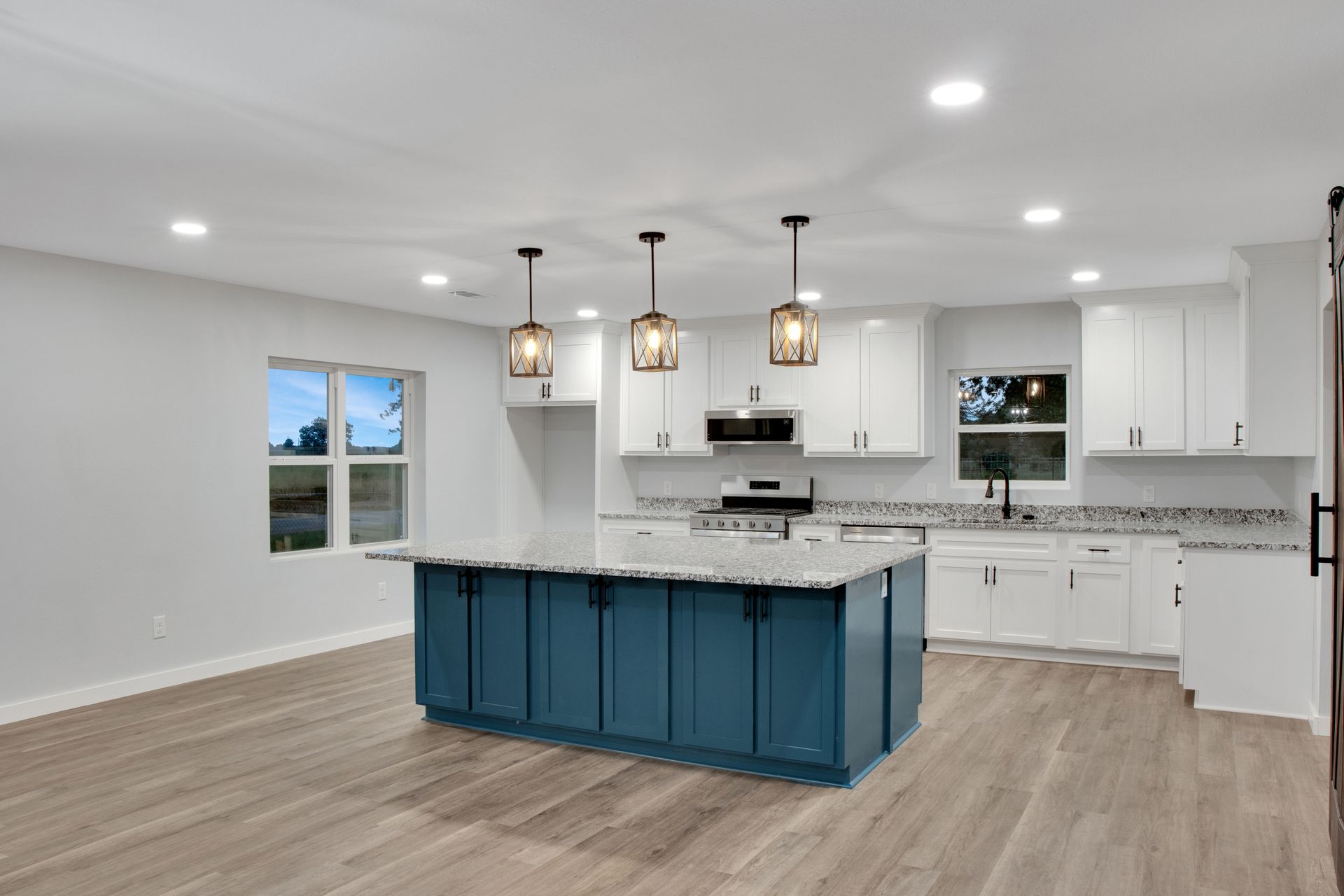 Modern kitchen with white cabinets, a blue center island, gray wood-look flooring, and pendant lights.