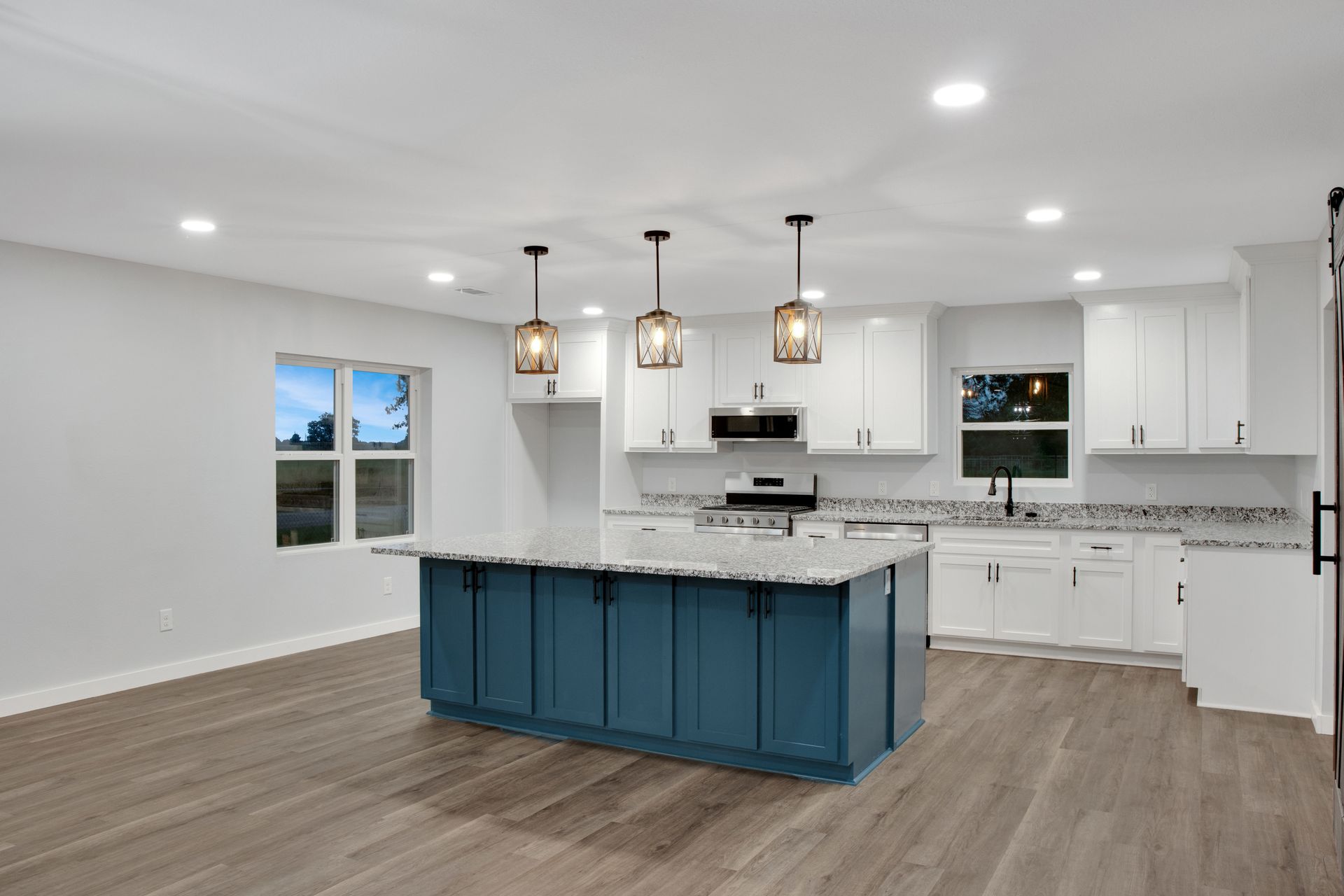 A modern kitchen featuring a teal island, white cabinets, grey wood-look floors, and three hanging pendant lights.