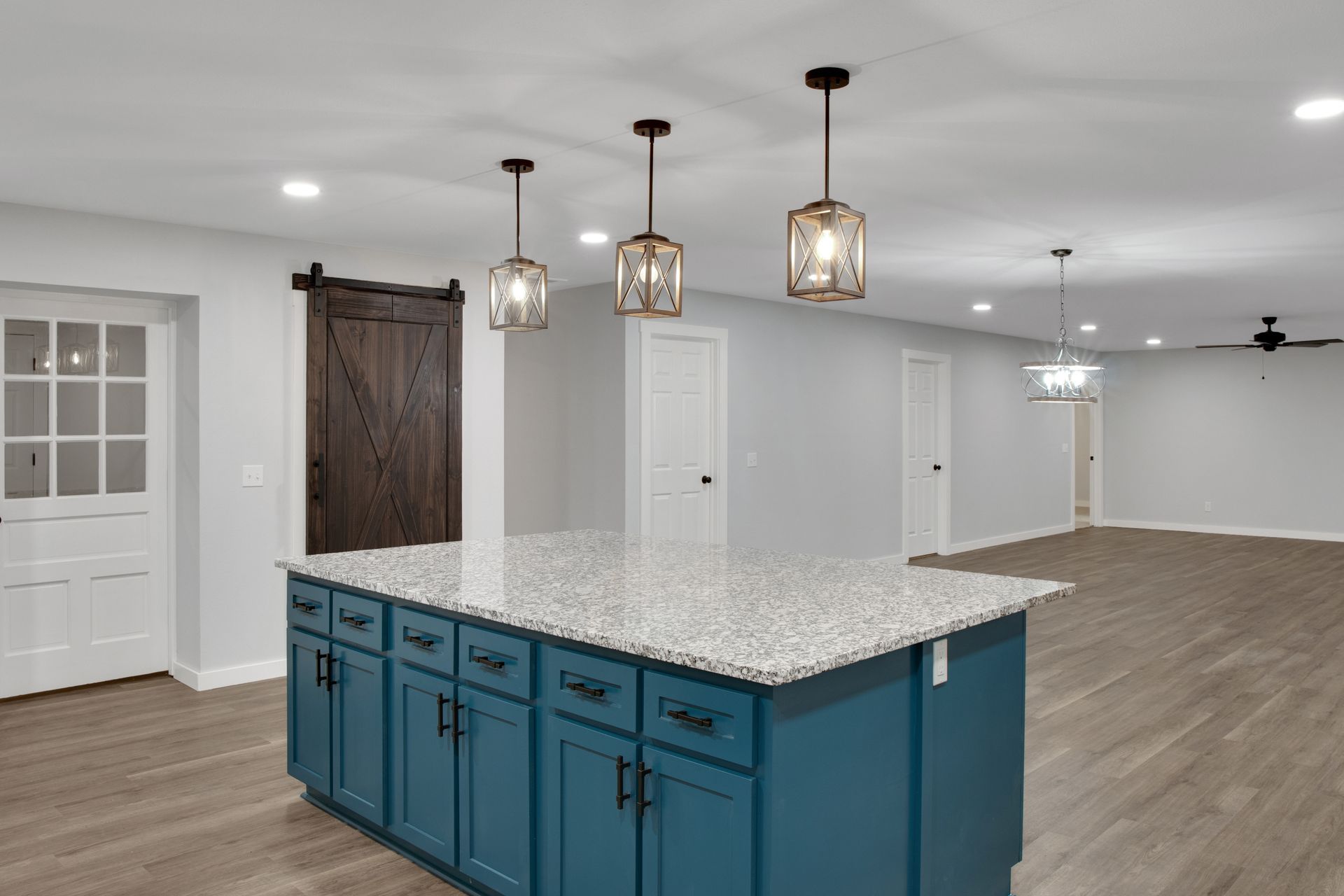 Modern kitchen featuring a blue center island with granite countertop, pendant lights, and a dark wood sliding barn door.