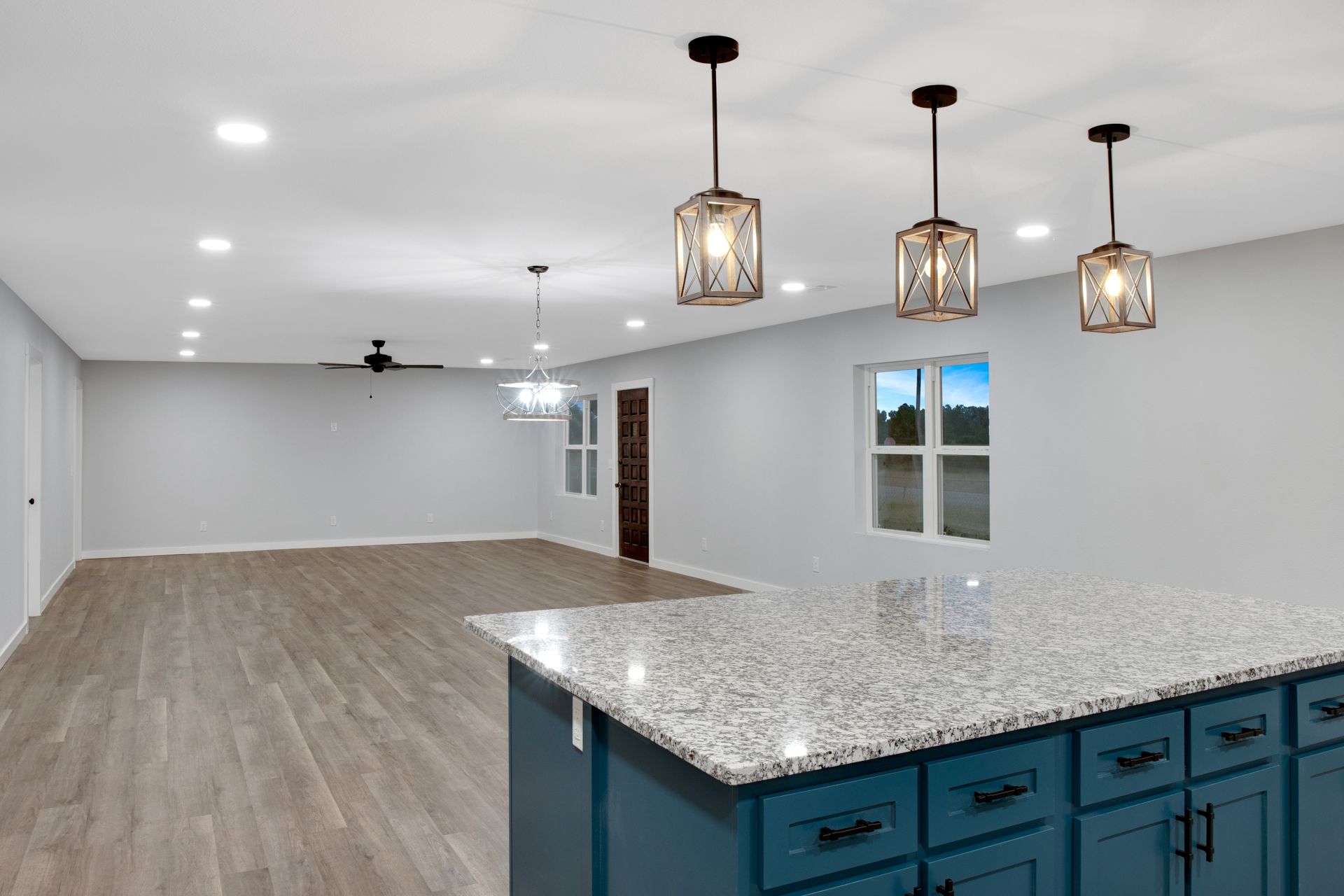 A kitchen island with blue cabinets and granite countertops, opening into a spacious room with light wood floors.