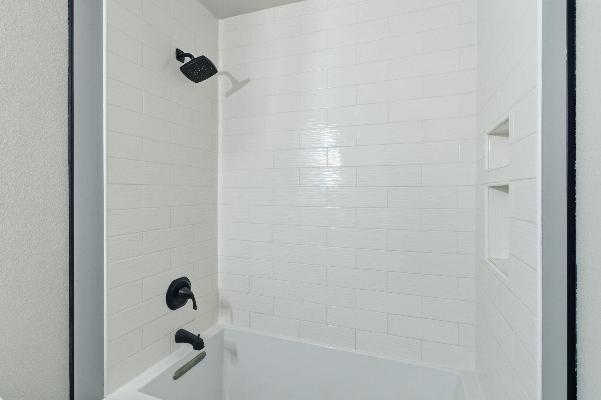 A shower and bathtub combination with white subway tile, a black showerhead, and matching black fixtures.