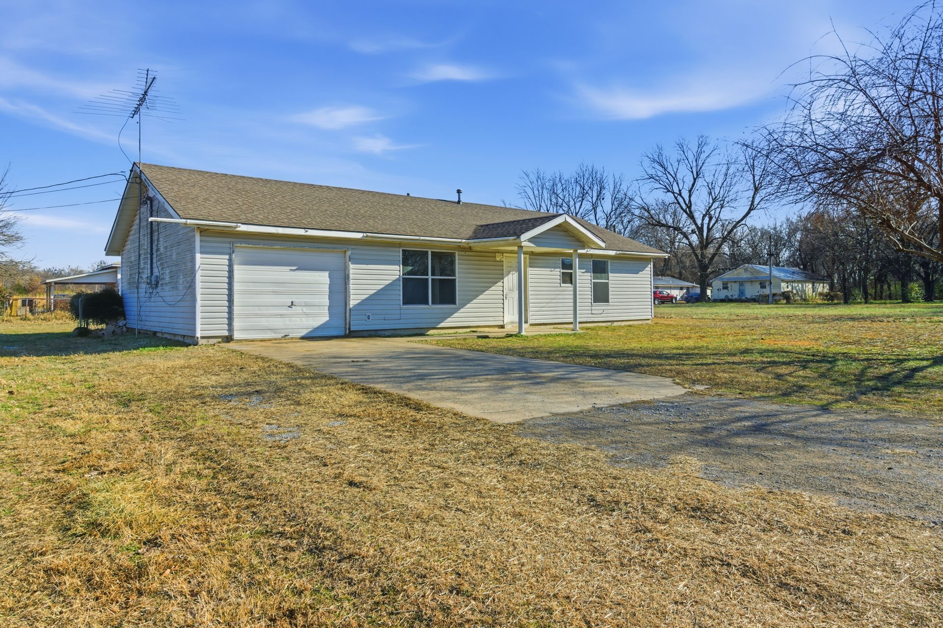 A single-story white house with a garage and a large front yard under a clear blue sky.