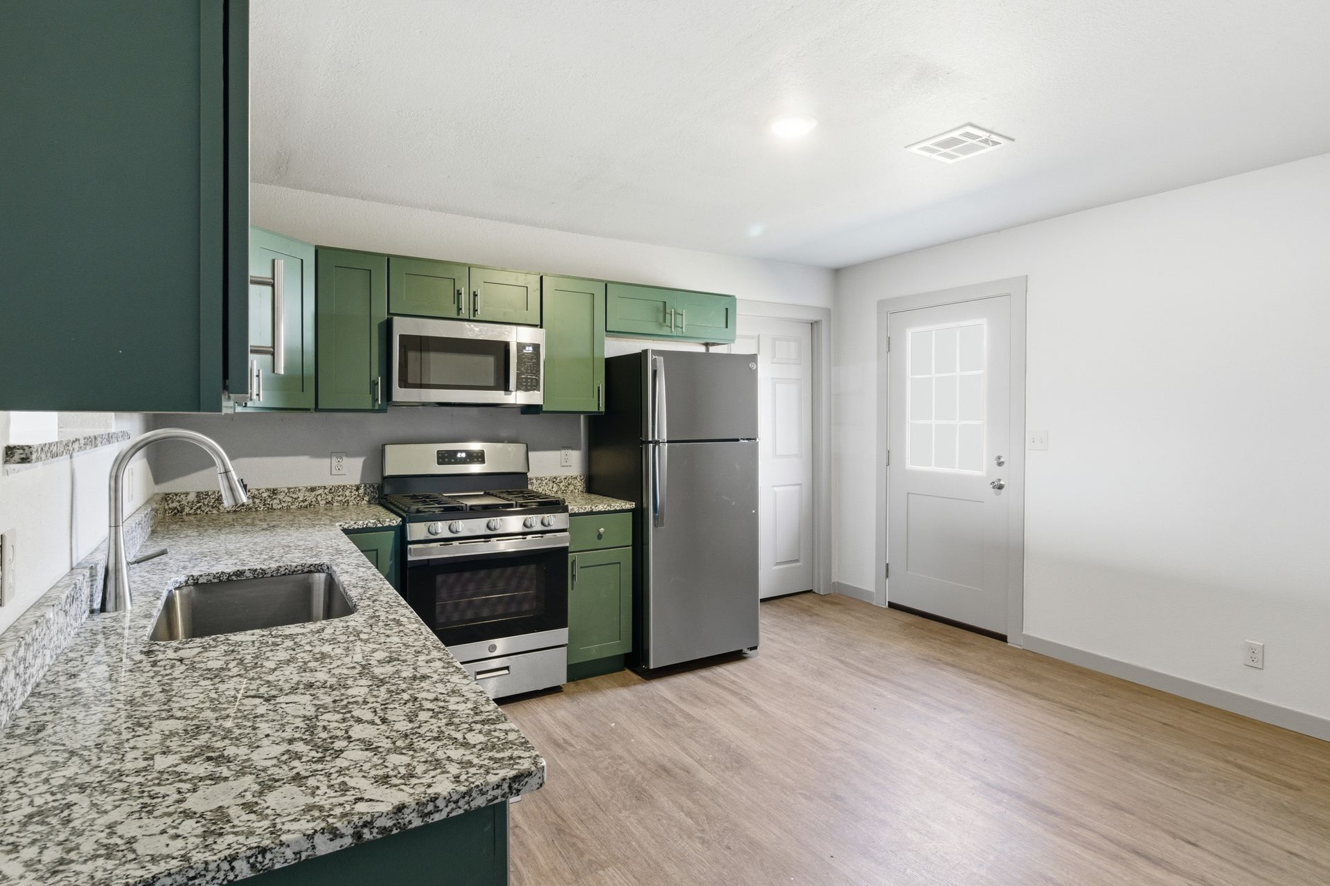 Kitchen with green cabinets, granite countertops, stainless steel appliances, and wood-style flooring.