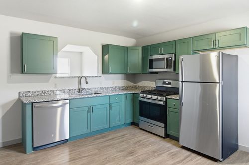 A kitchen with sage green cabinets, light wood flooring, granite countertops, and stainless steel appliances.