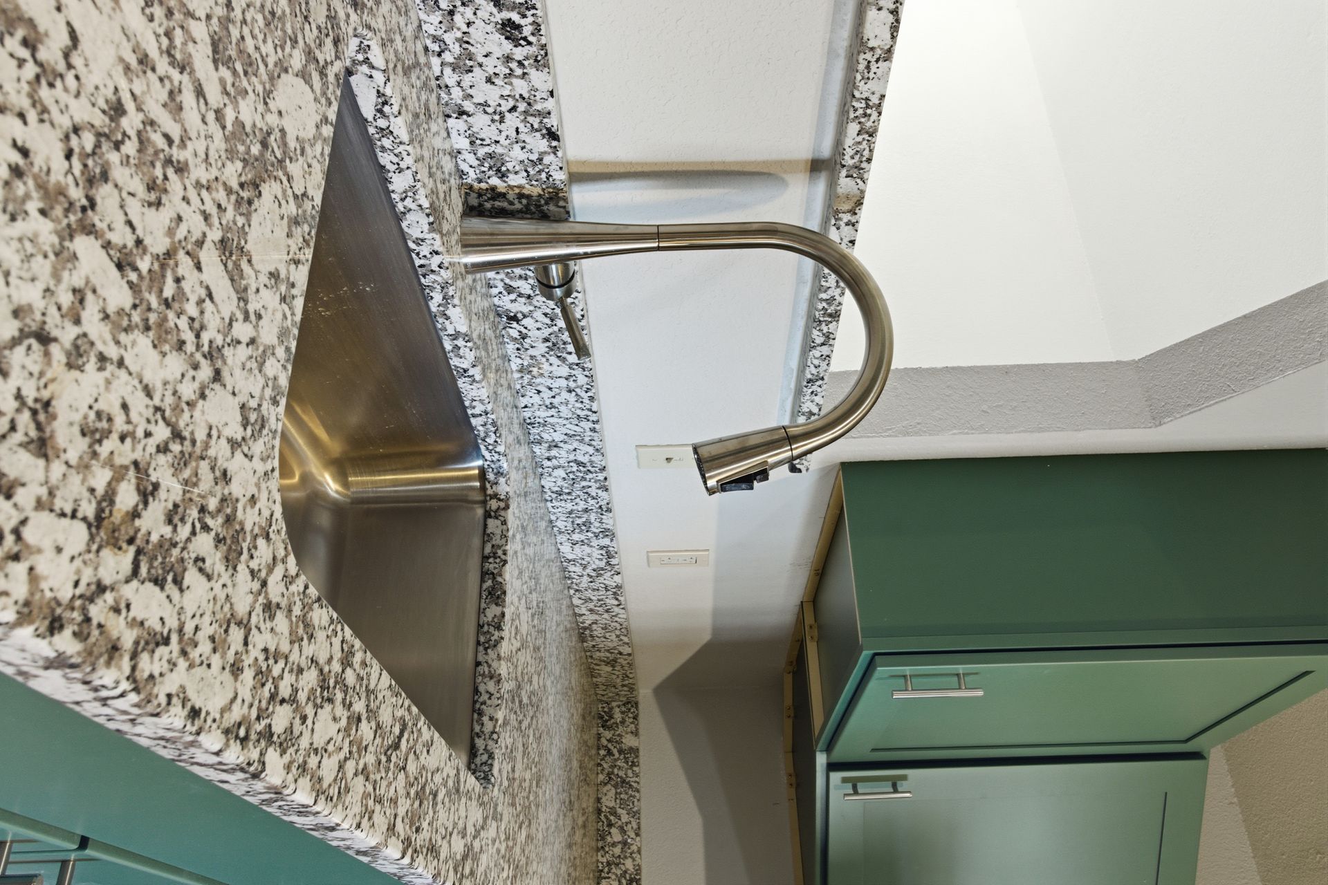 An overhead view of a kitchen sink with a stainless steel faucet set into a speckled granite countertop.