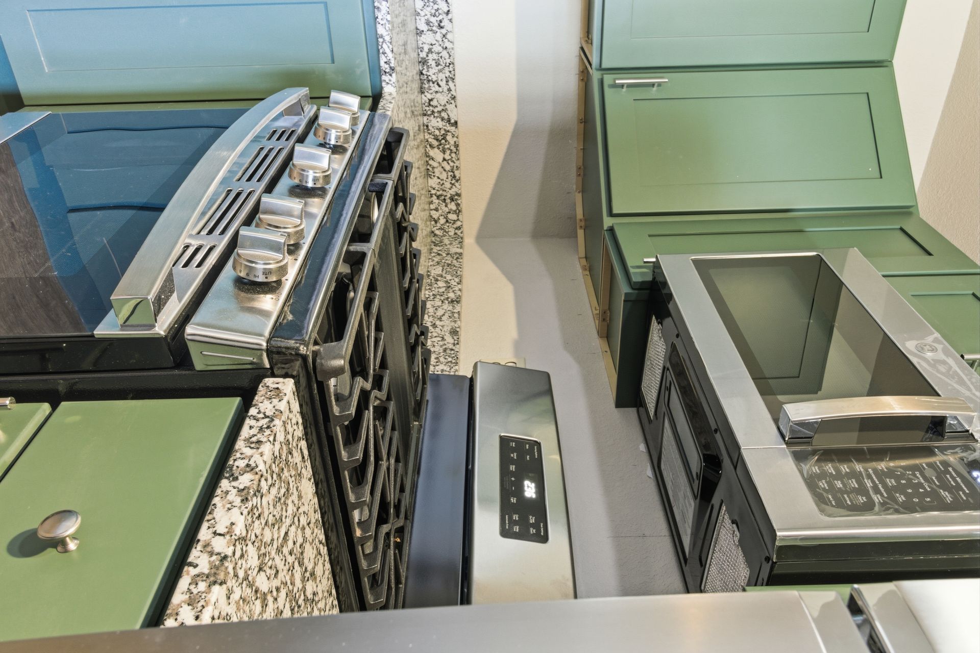An overhead view of a kitchen workspace featuring a black oven, green cabinetry, and stainless steel appliances.