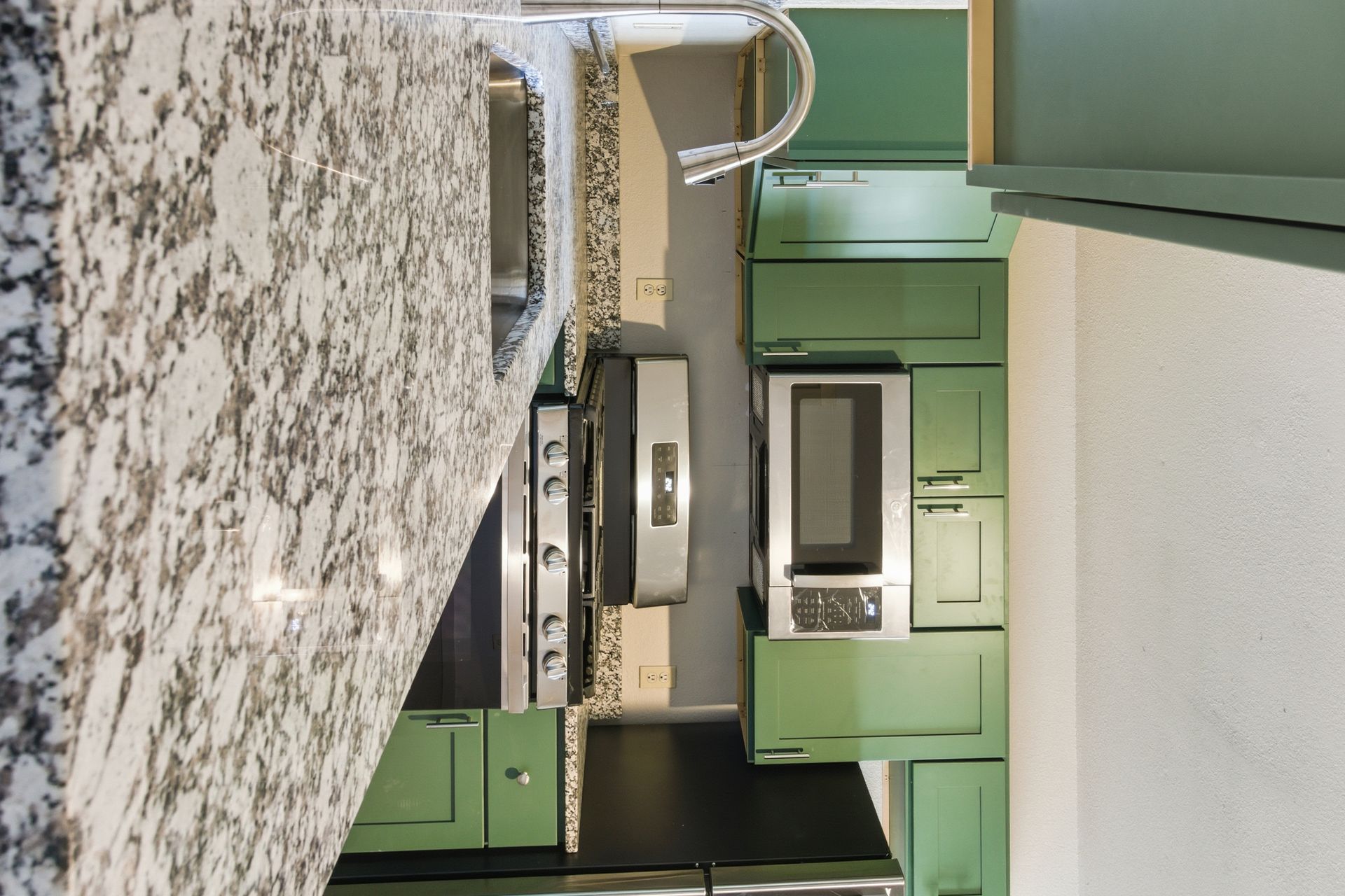 A kitchen featuring sage green cabinets, light granite countertops, a stainless steel gas range, and a built-in microwave.