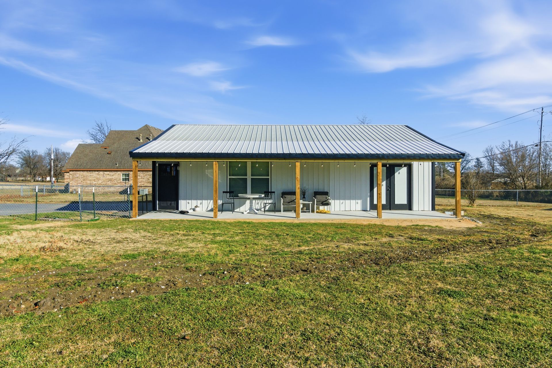 A single-story white house with a metal roof and front porch, set in an open grassy field under a clear blue sky.