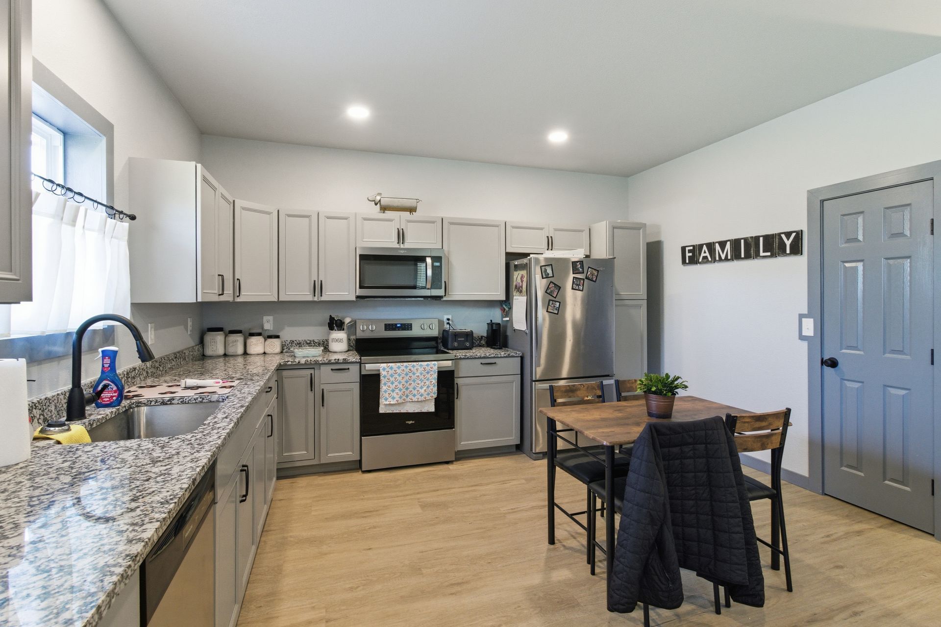 A light gray kitchen with granite countertops, stainless steel appliances, and a small dining table with chairs.