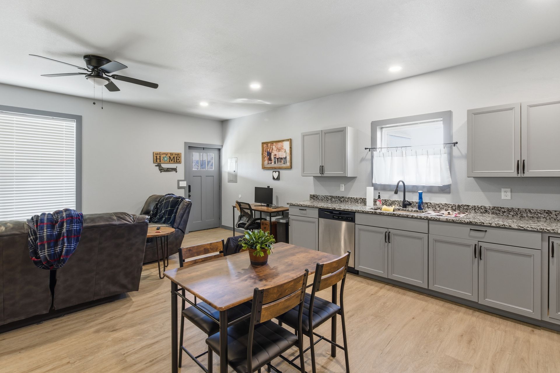 A gray-toned open-concept kitchen and living area featuring a wooden dining table, gray cabinets, and a sofa.