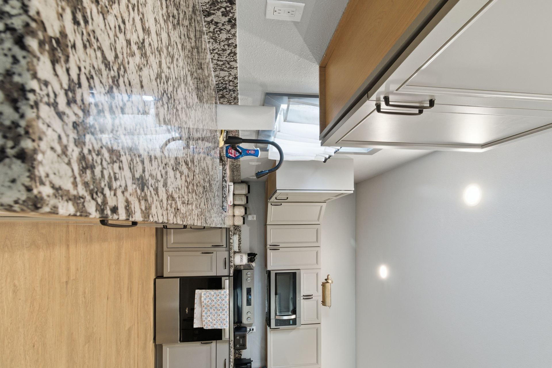 A granite countertop kitchen with light-colored cabinets, stainless steel appliances, and a paper towel holder.