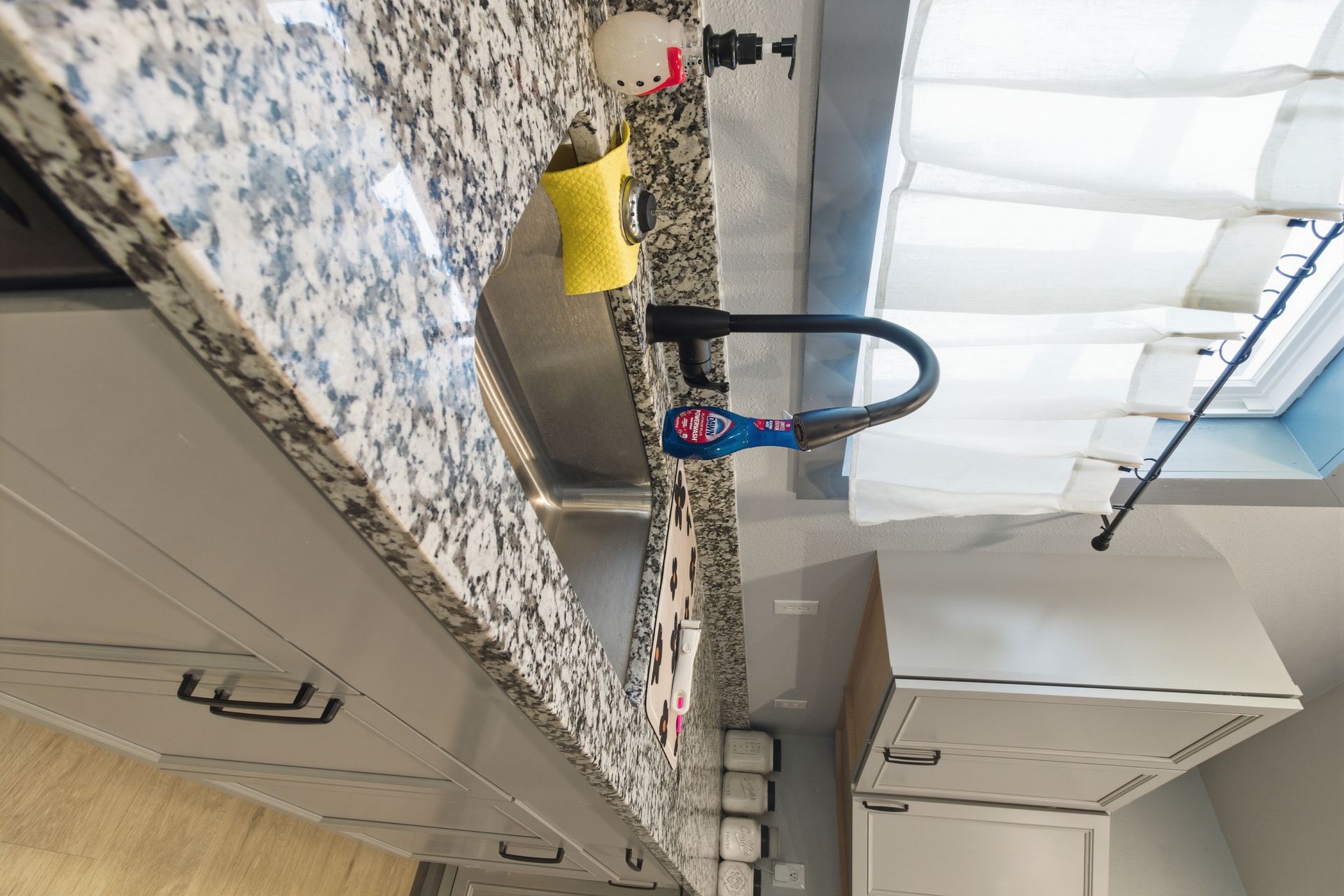 A kitchen sink area featuring a grey countertop with a granite pattern, a black faucet, and a sponge next to the basin.