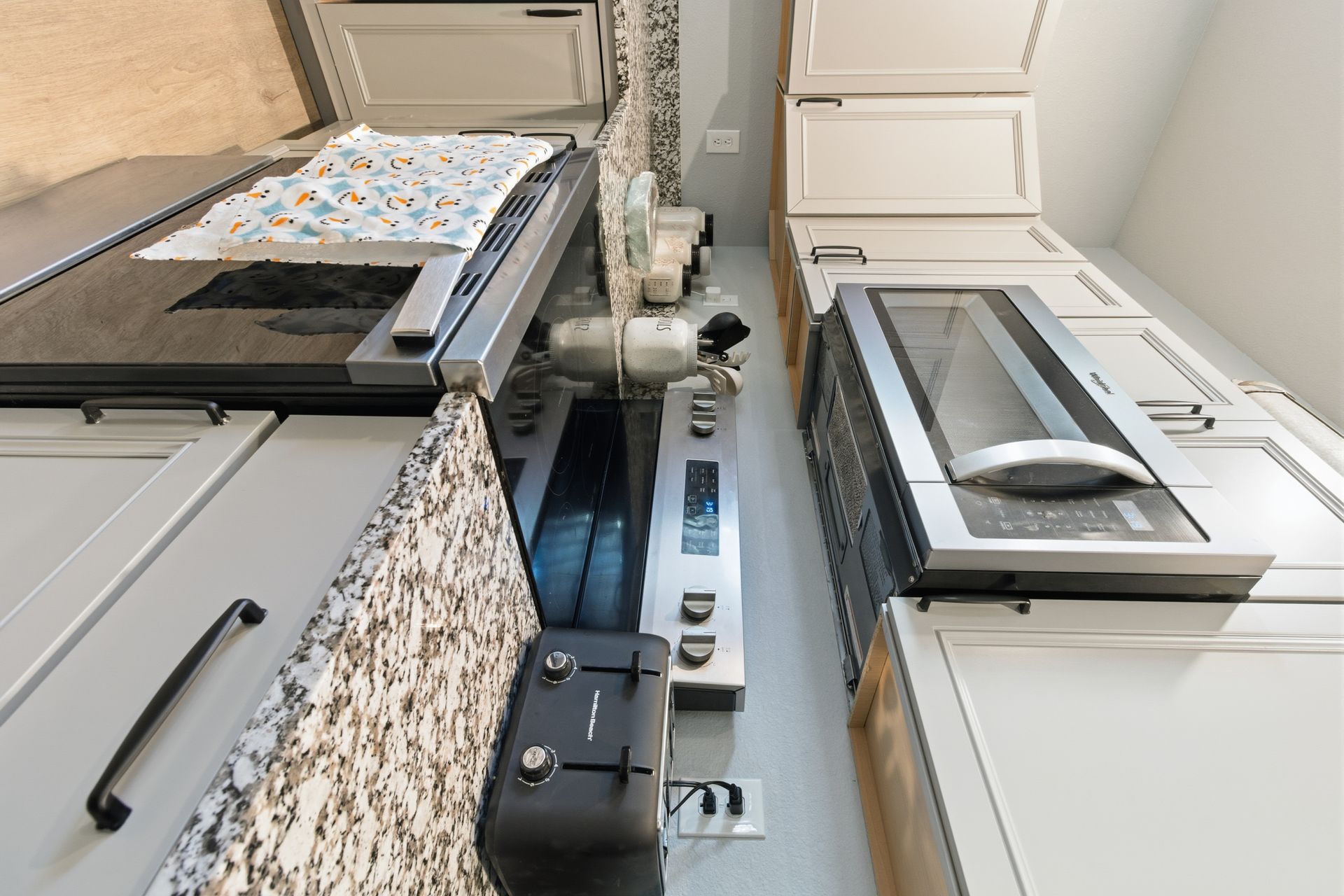 A kitchen workspace with gray cabinets, granite countertops, a stove, a toaster, and a built-in microwave.