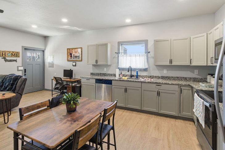 Open-plan kitchen and dining area with light grey cabinets, granite countertops, a wood table, and a grey entry door.