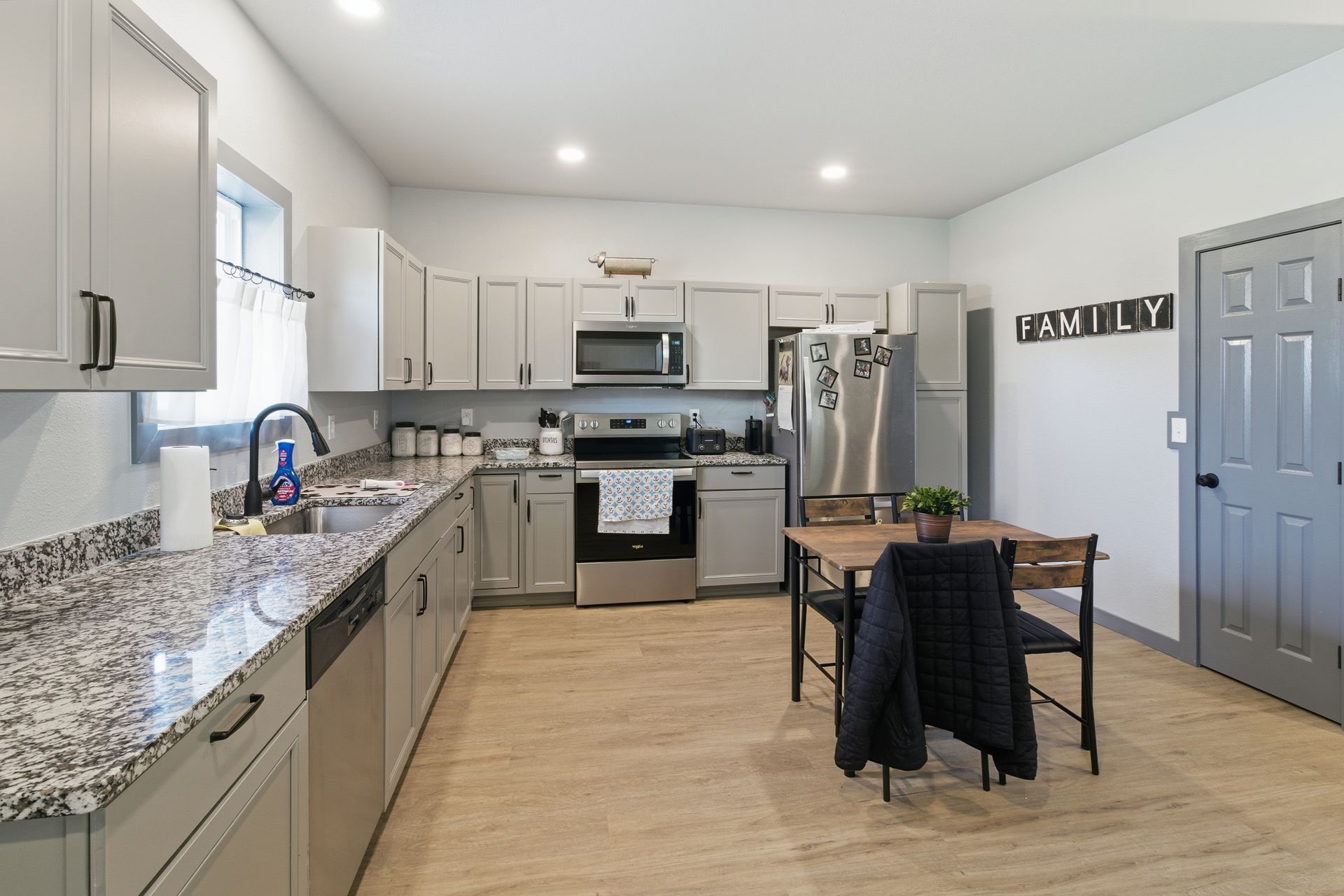 Modern kitchen with gray cabinets, granite countertops, stainless steel appliances, and a small dining table.