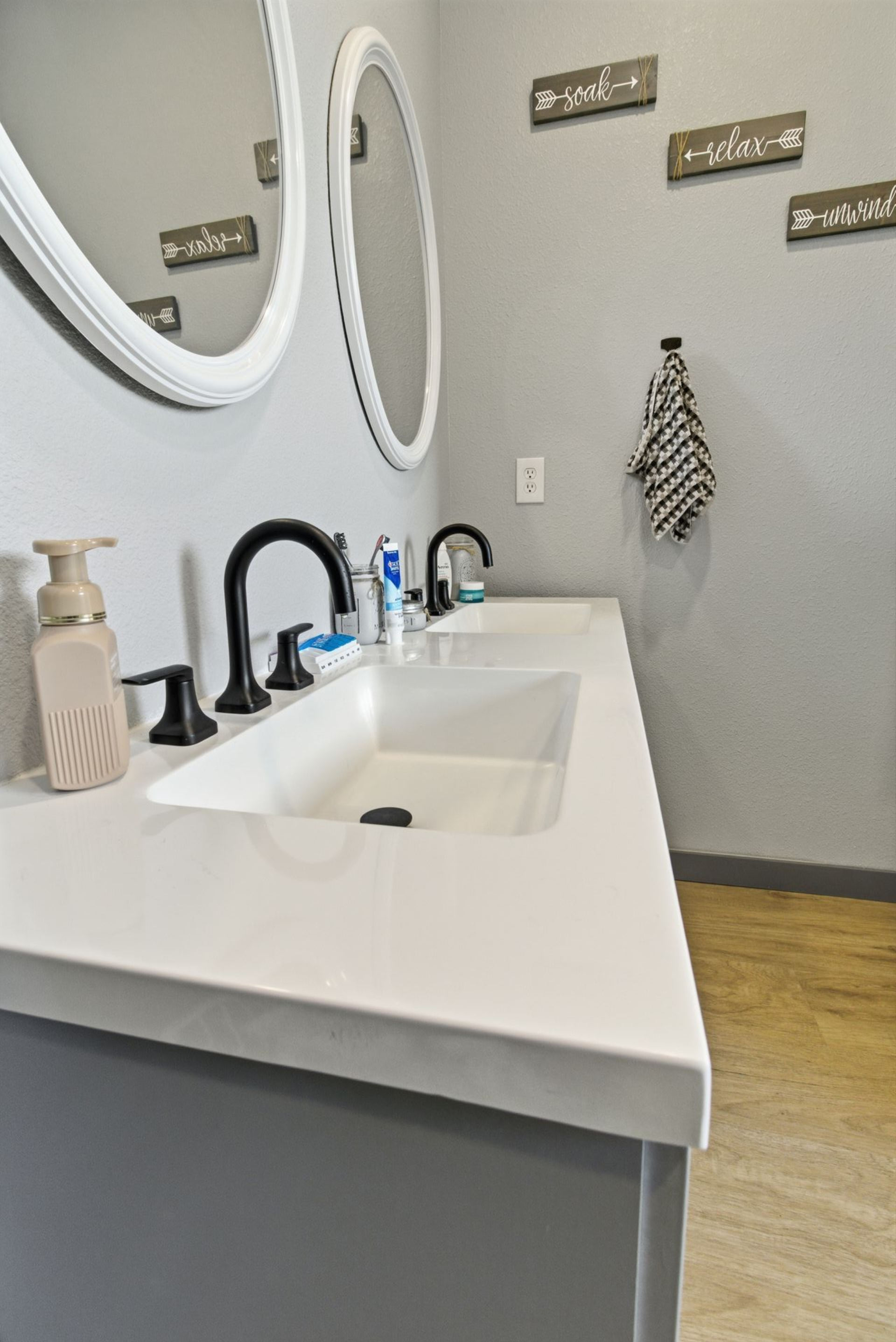 Modern bathroom vanity with white sink, black faucet, round mirror, and wall hooks in a gray room