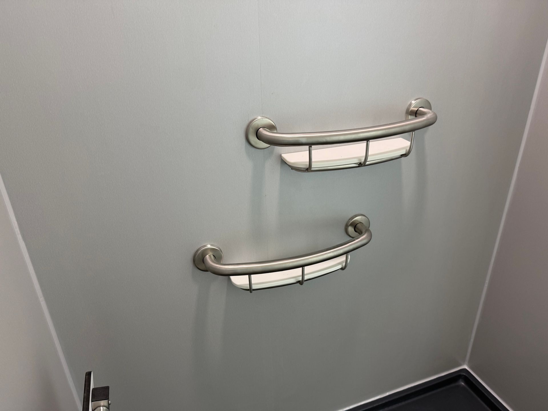 Two stainless-steel Fibo grab bars mounted on a light gray wall above a tiled corner.