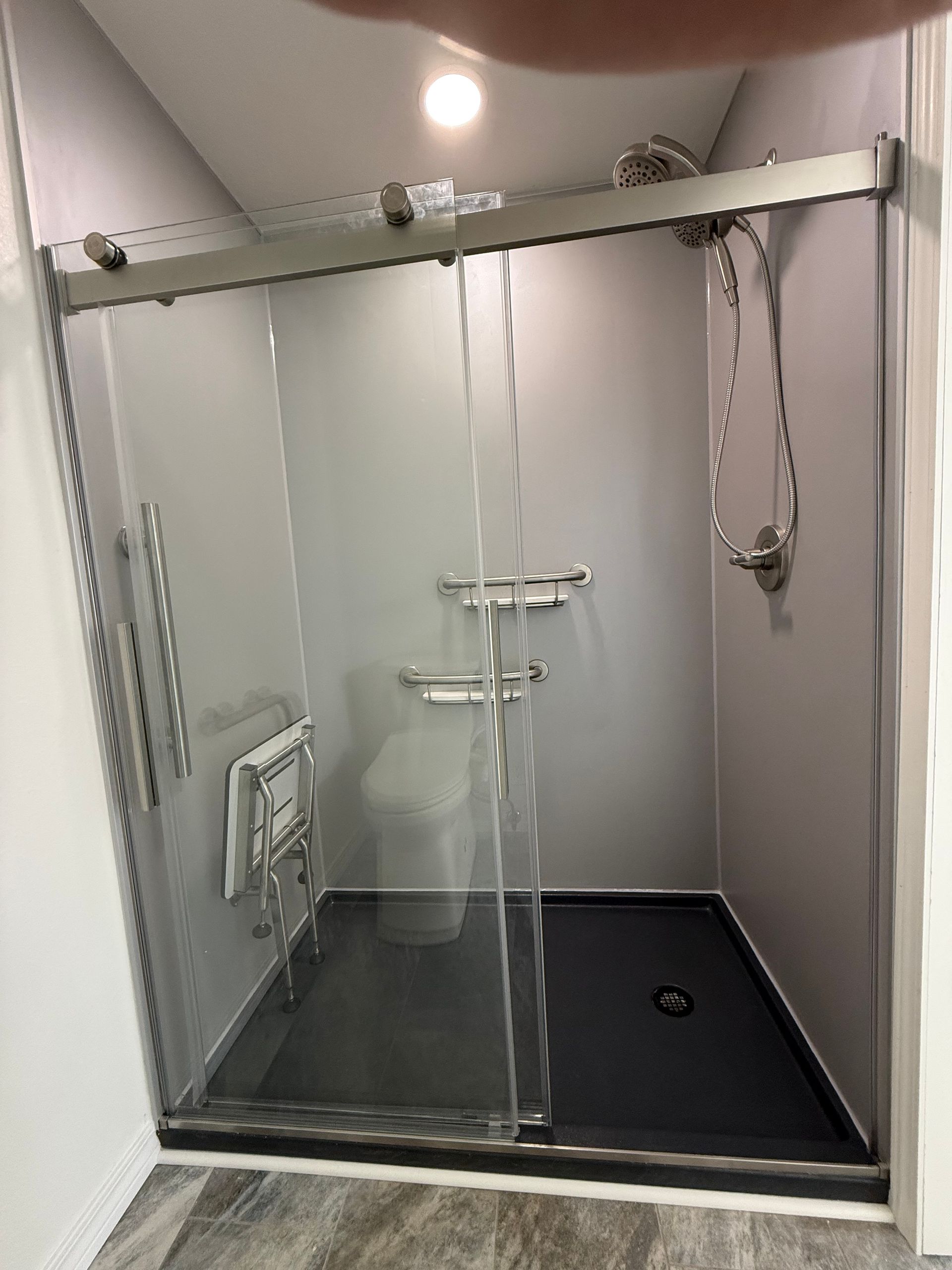 Glass shower stall with two showerheads and a dark floor, viewed from the outside