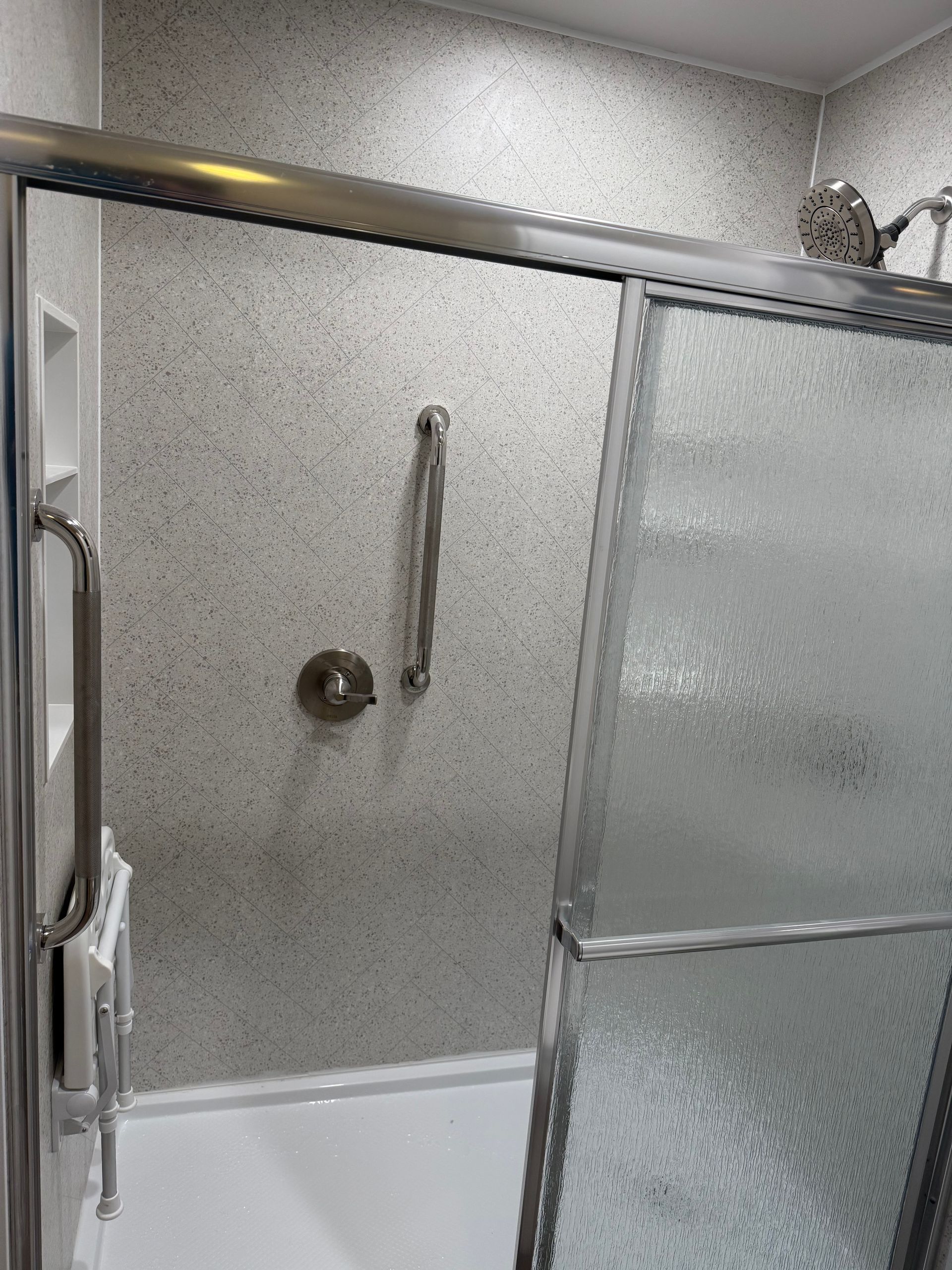 Small tiled Fibo shower with frosted glass doors and chrome grab bars in a bathroom