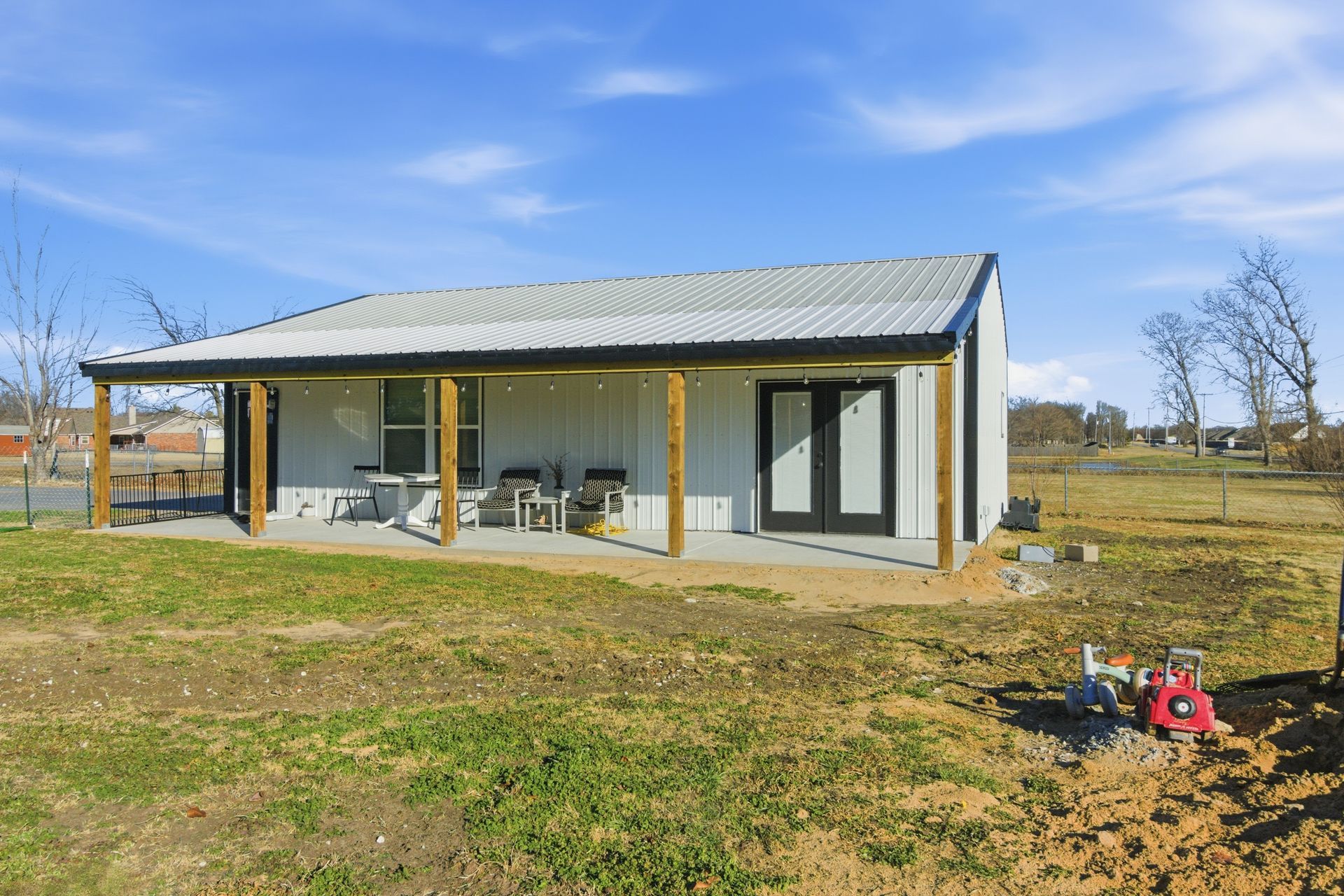 A white metal-sided building with a covered front porch, glass doors, and a metal roof in a grassy, rural setting.