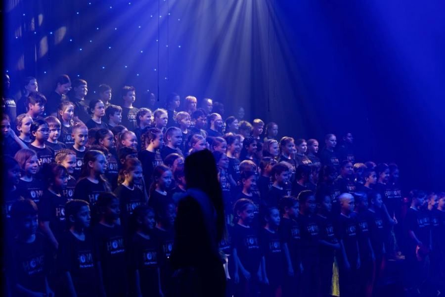 A woman is standing in front of a large choir on a stage.