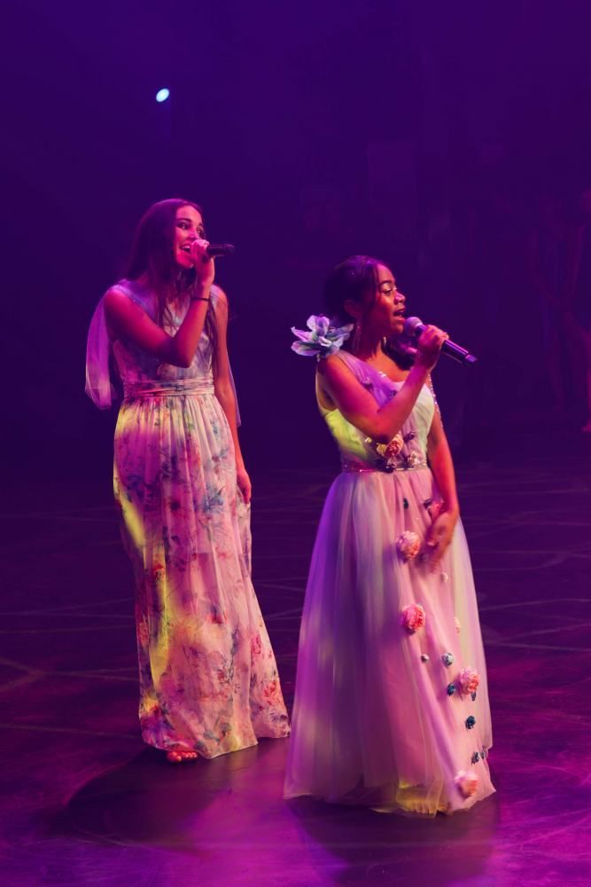 Two women are singing into microphones on a stage.