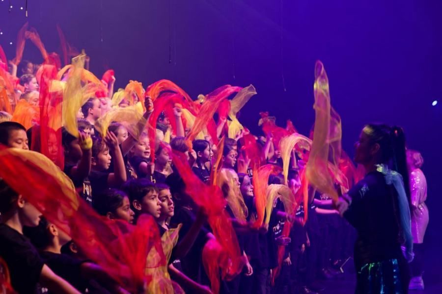 A woman is standing in front of a crowd of people holding colorful scarves.