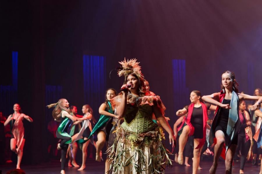 A woman is singing into a microphone in front of a group of dancers on a stage.