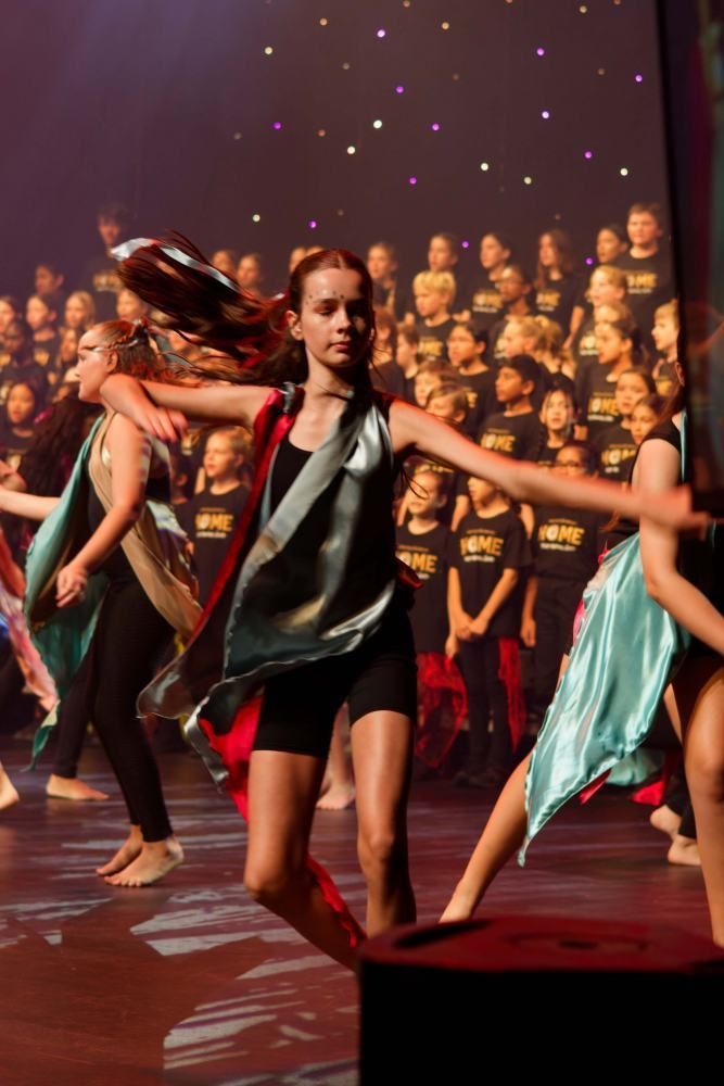 A group of young girls are dancing on a stage in front of a choir.
