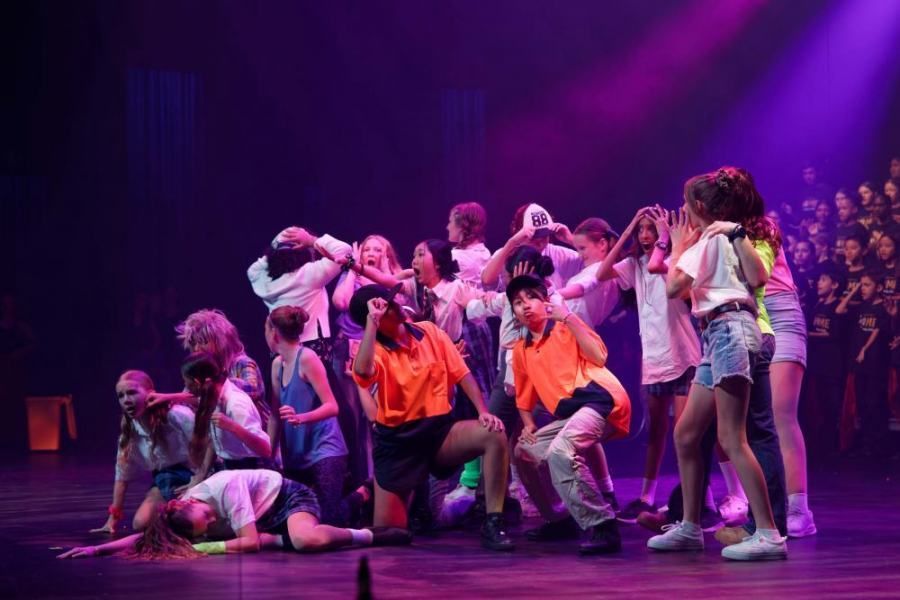 A group of young people are dancing on a stage in front of a crowd.