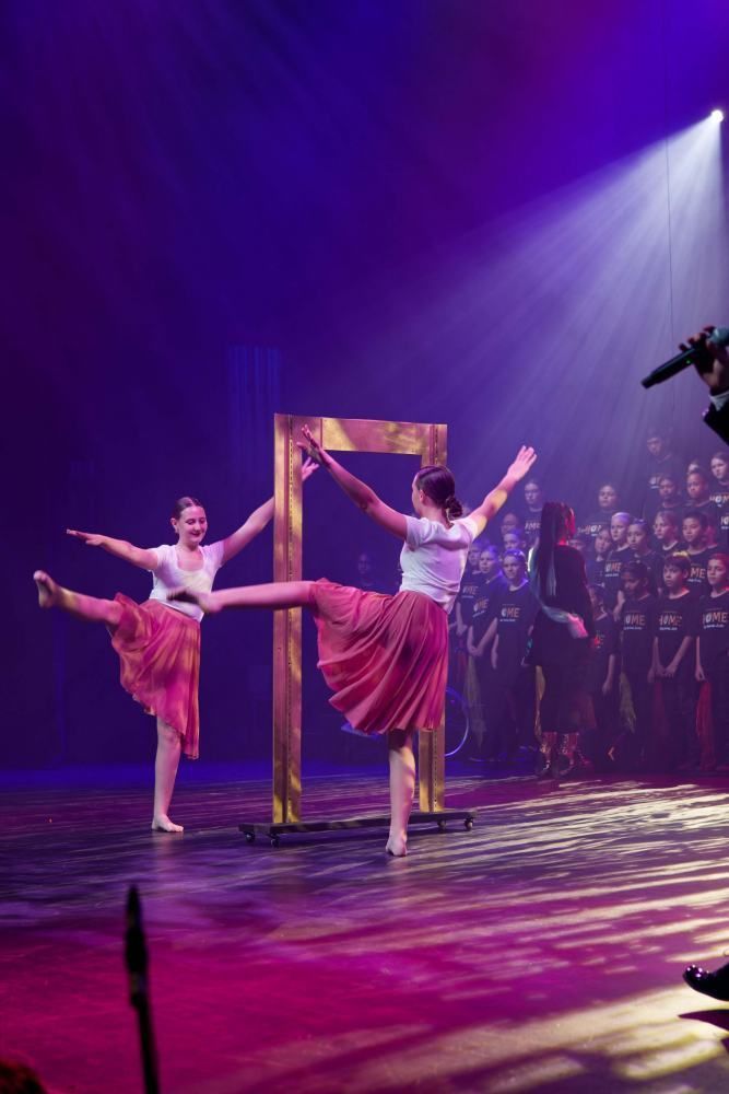 Two dancers are dancing on a stage in front of a choir.