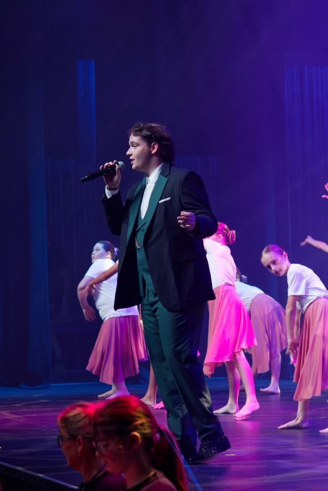 A man in a tuxedo is singing into a microphone on a stage.