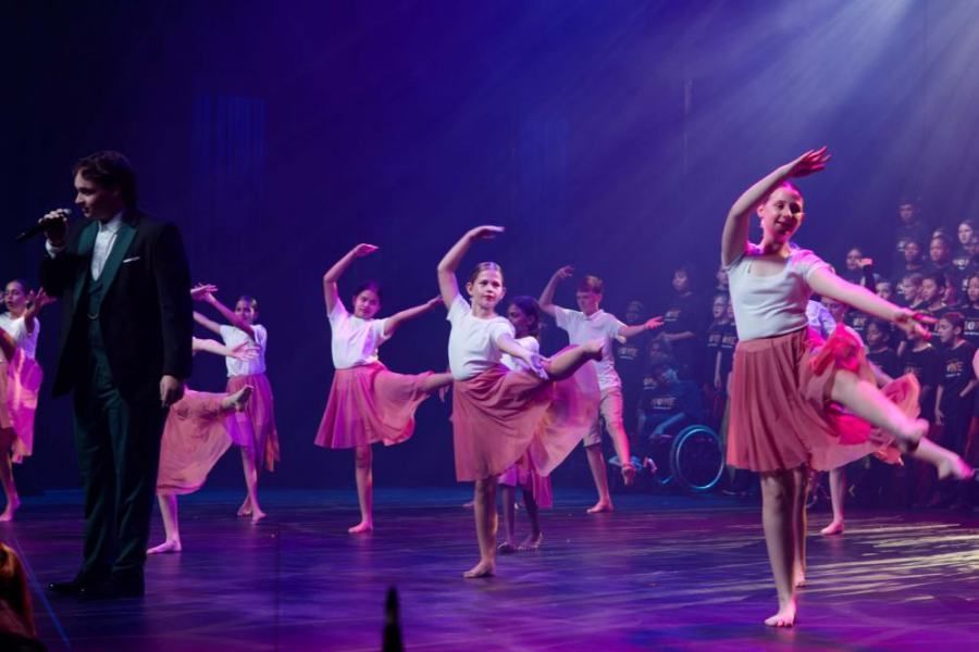 A group of dancers are performing on a stage while a man sings into a microphone.