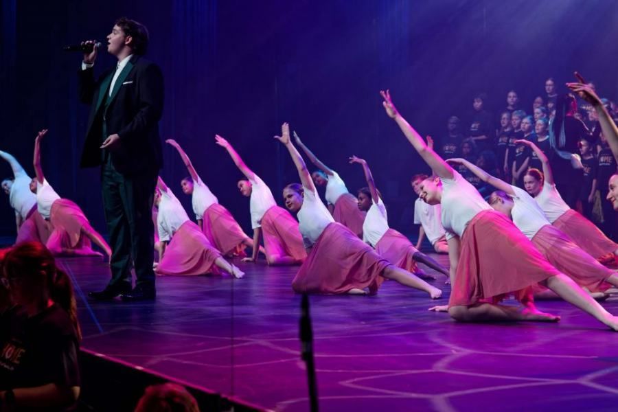 A man is singing into a microphone in front of a group of dancers on a stage.