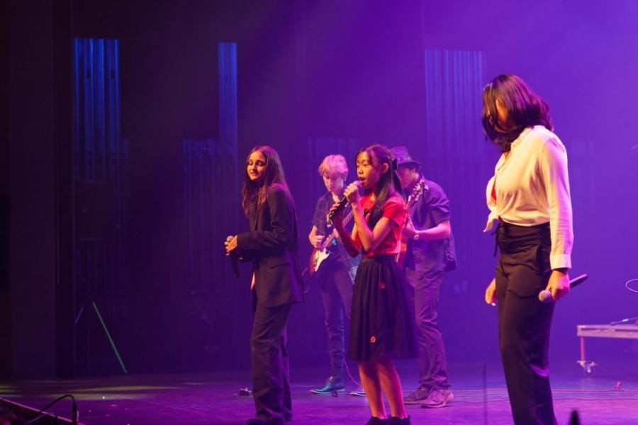 A group of people are standing on a stage singing into microphones.