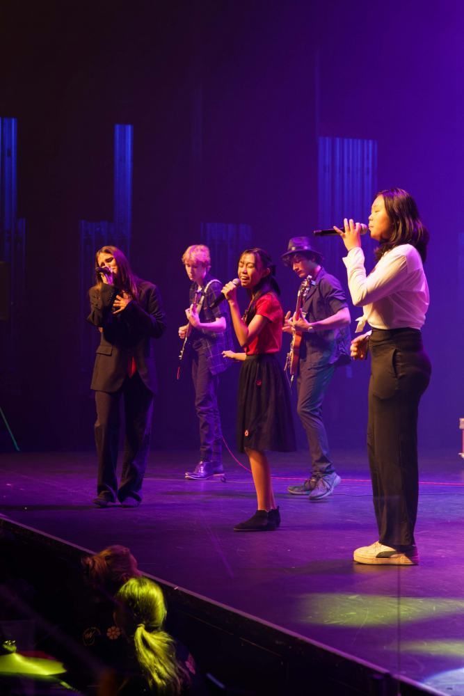 A group of people are standing on a stage singing into microphones.