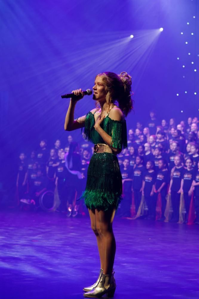 A woman in a green dress is singing into a microphone on a stage.