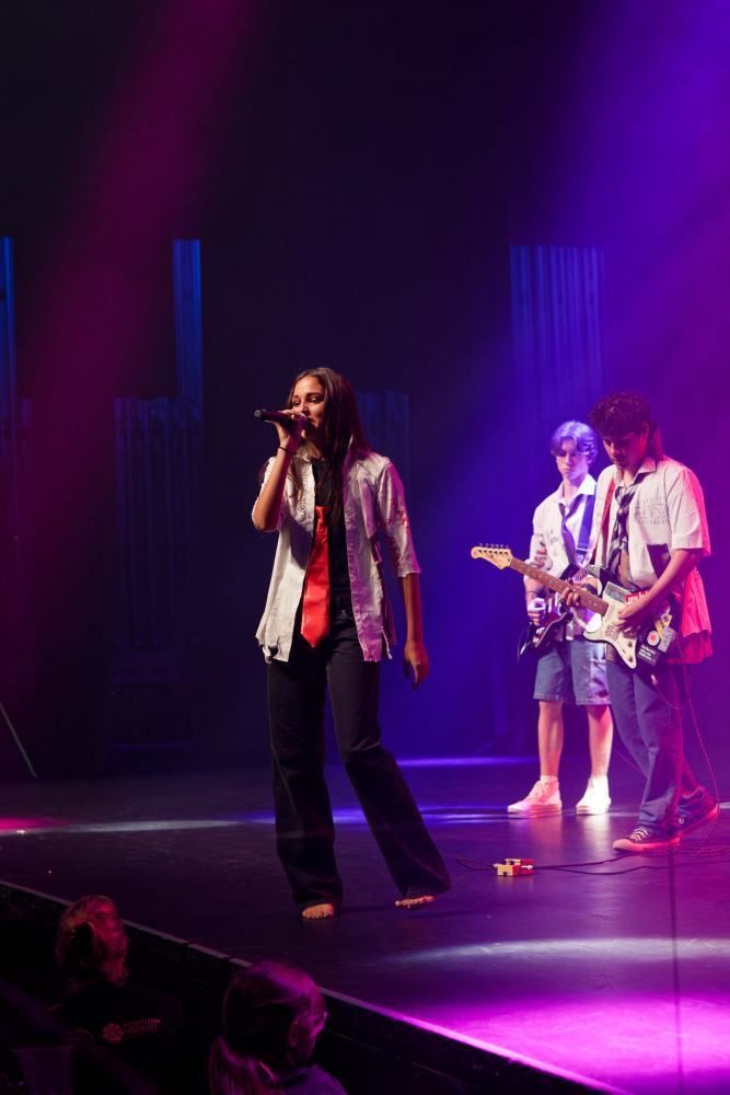 A woman is singing into a microphone while two men play guitars on stage.