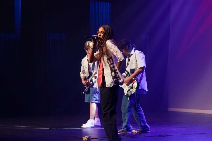 A woman is singing into a microphone while two men play guitars on a stage.