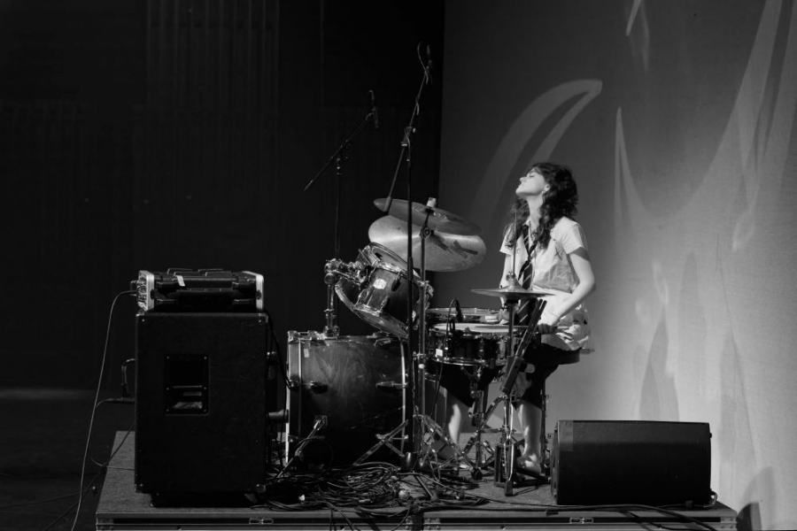 A woman is playing drums on a stage in a black and white photo.