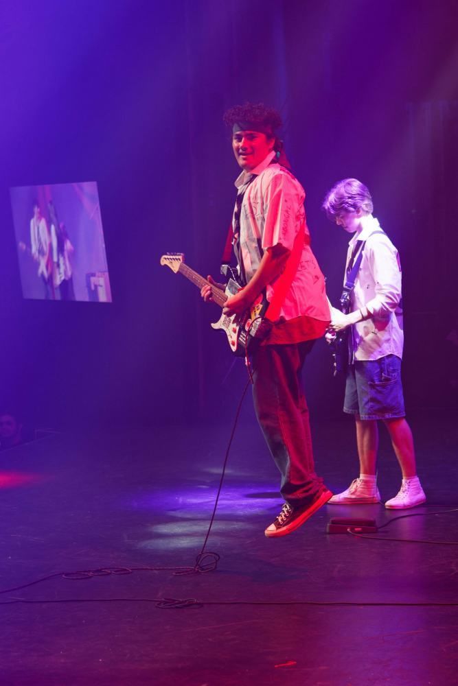 Two men are playing guitars on a stage with purple lights