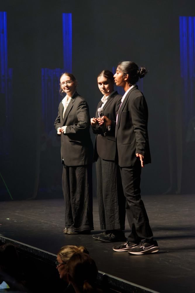 Three people in suits are standing on a stage.