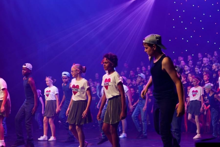 A group of children are dancing on a stage in front of a crowd.