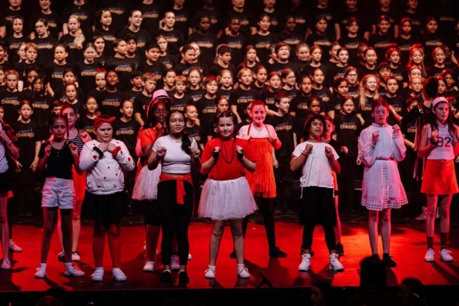 A group of children are standing on a stage in front of a large choir.