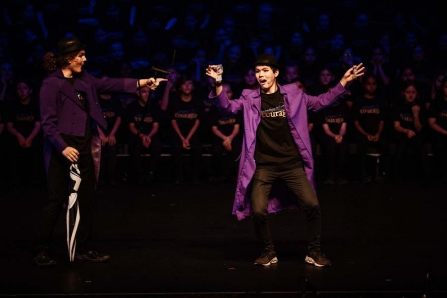 A man in a purple coat is dancing on a stage in front of a crowd.