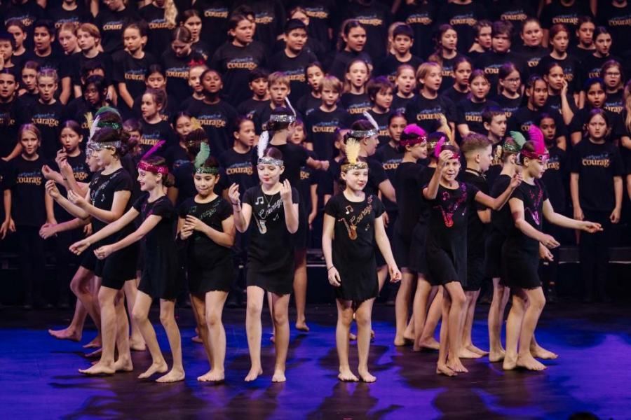 A large group of children in black shirts are dancing on a stage.